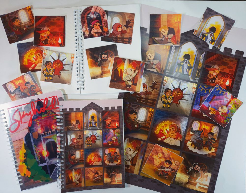 A selection of scattered items including a sketchbook, a reusable sticker book, poster prints, and vinyl stickers all featuring the companions and the locale Skyhold from Dragon Age Inquisition