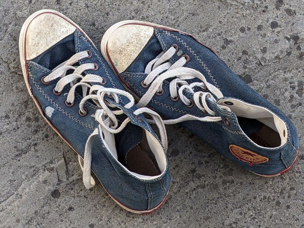 a pair of blue denim Converse Chuck Taylor All Star High-Top trainers shoes that are getting old and fraying at the edges - like their owner . . !