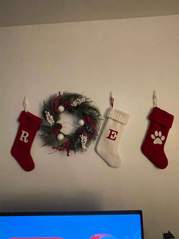 Christmas stockings and a Christmas wreath above a TV playing Nintendo winter music. 