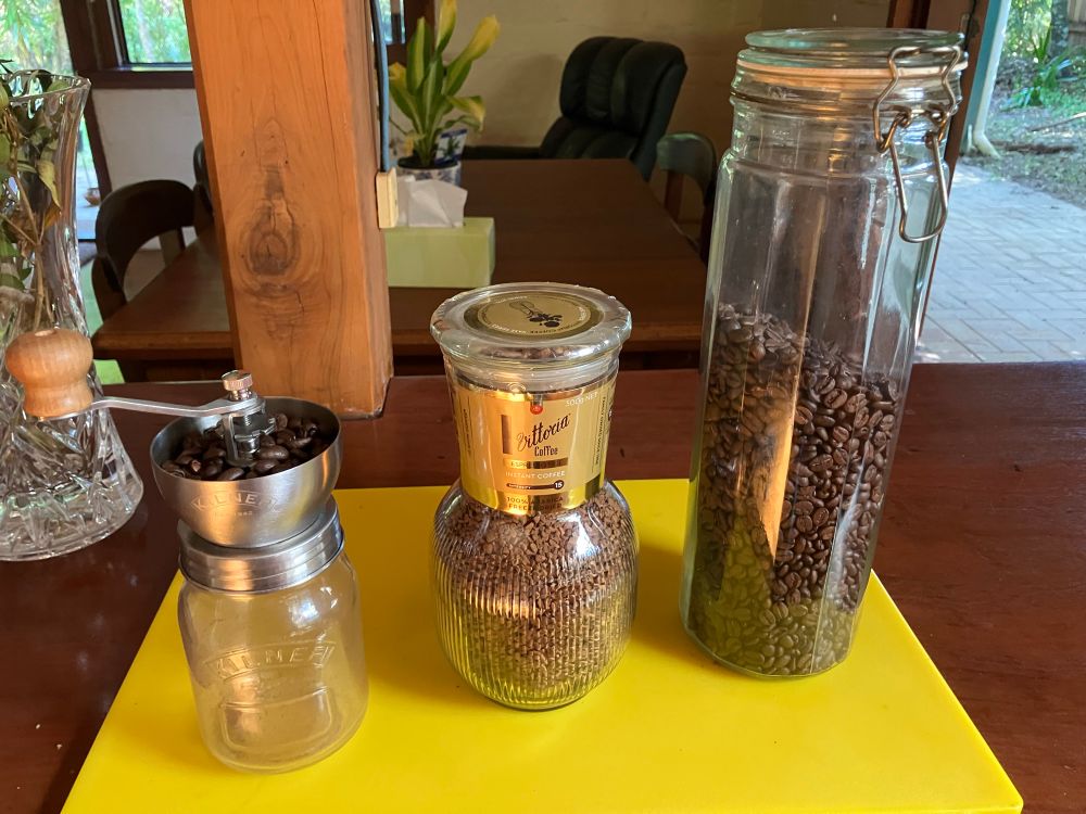 A hand coffee grinder, a fancy looking jar of instant coffee and a jar of coffee beans 