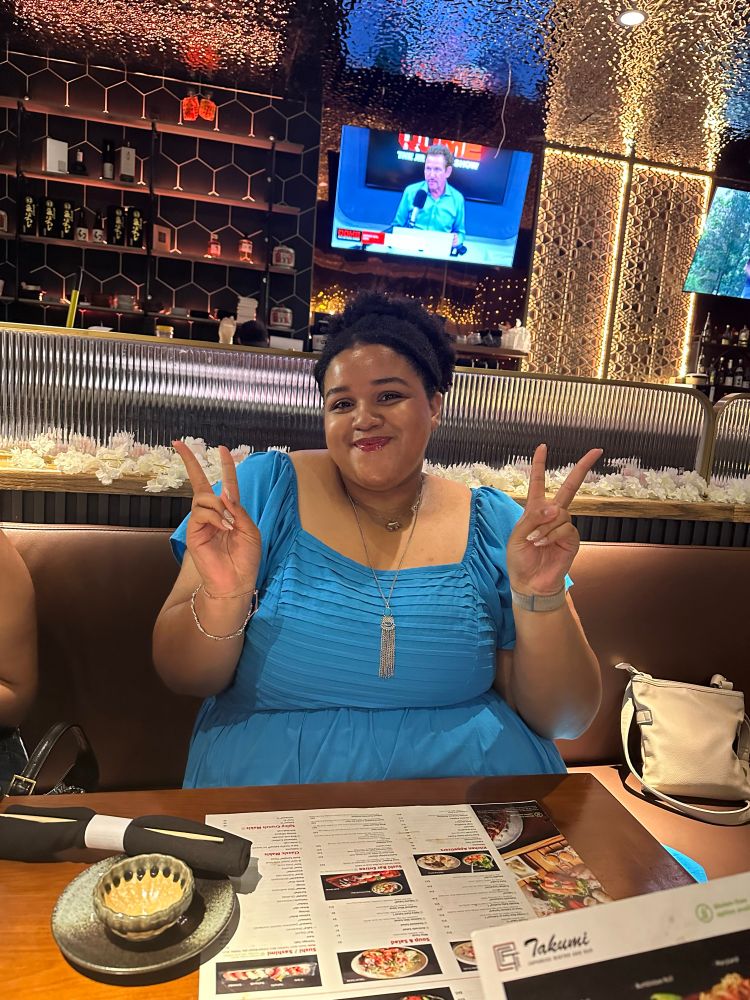 A photo of myself at a Japanese restaurant wearing a blue dress, holding up two peace signs and smiling 