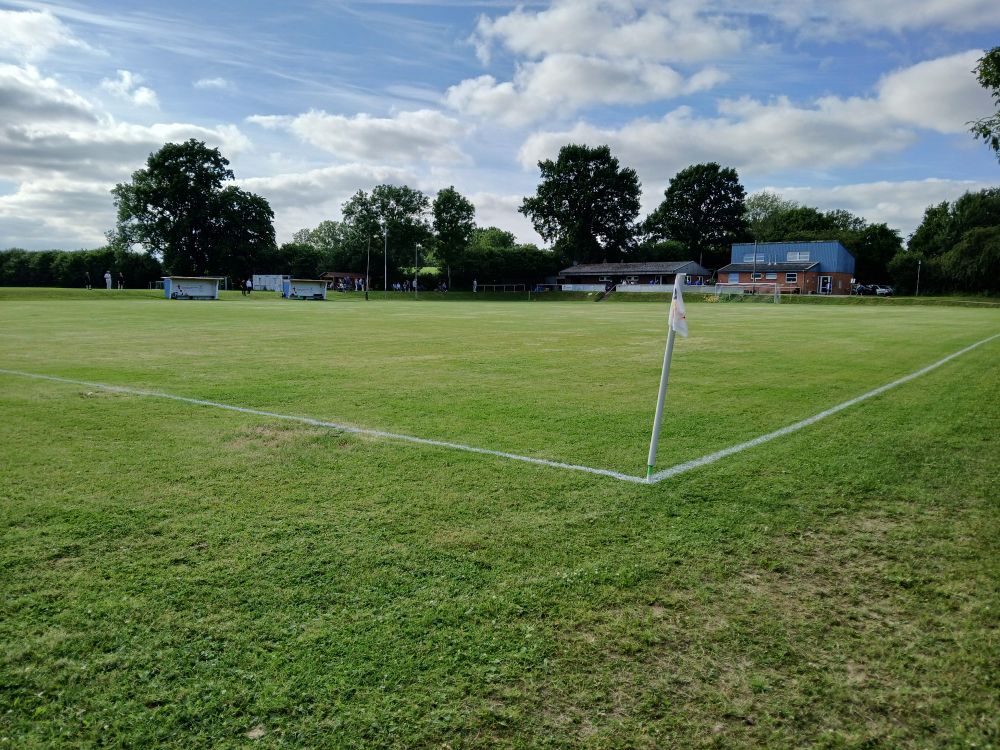 Spielfeld der Sportplatz Karkkamp in Melsdorf mit Trainerbänken und Vereinsheim im Hintergrund. 
