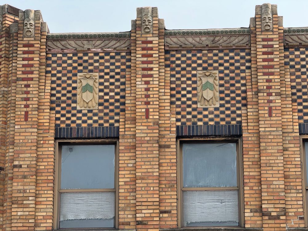Color close-up of another set of windows on the side elevation. Again we have faces atop piers with an arrangement of red bricks that serve to emphasize the building's verticality, but between them are a different shield centered in a bed of brick laid in a checkerboard pattern underneath a stylized Art Deco sunburst of cast stone.