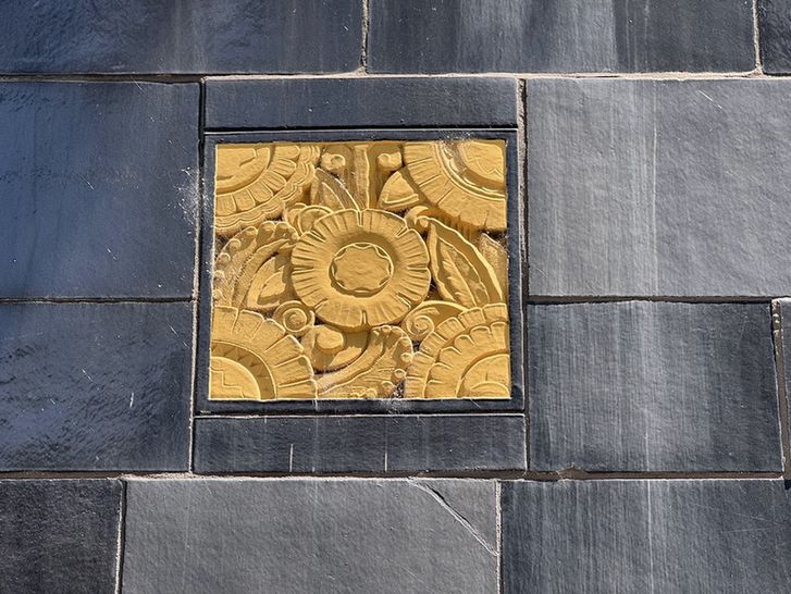 Color detail of a golden Art Deco panel featuring stylized floral and geometric designs surrounded by black terra cotta.