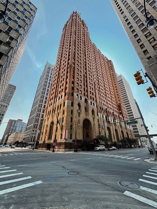 Wide angle color photo of a tan granite and orange brick skyscraper, taken on an angle from across the intersection. No real details can be noted beyond its immensity. 