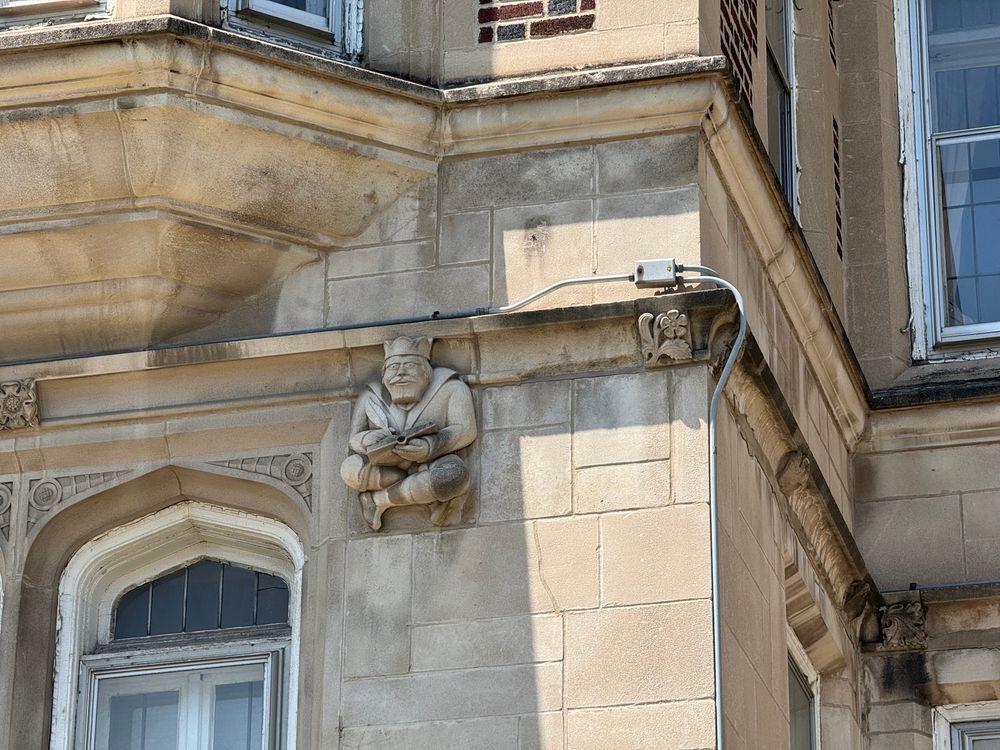 Color close-up of part of the facade where a little guy in a crown and robes sits, staring angrily ahead as he writes no doubt unpleasant things in his little stone book.