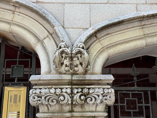 Color close-up of part of the entrance to a building. Where two arches meet sit two adorable little dragons, almost, but not quite touching cheeks and sitting on little carved leaves and flowers.