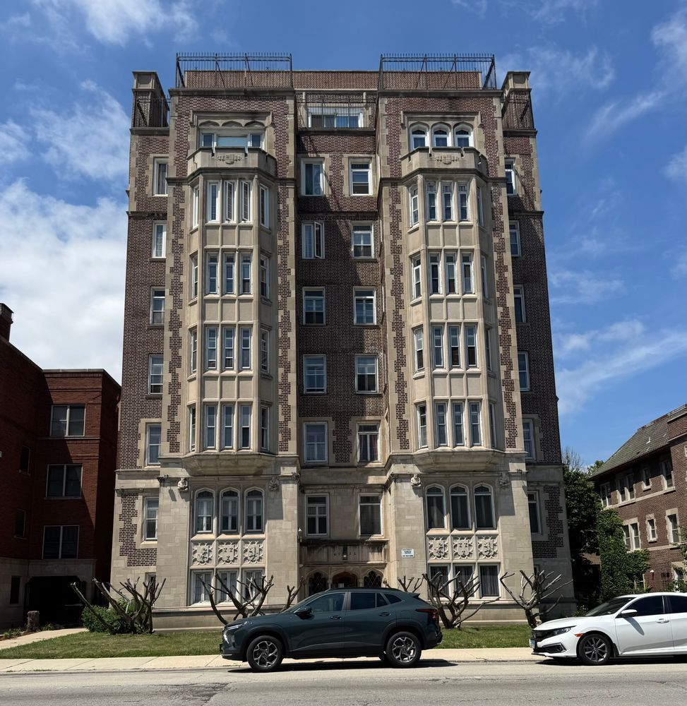 Color photo of an eight story brick apartment building with a flat roof, stone accents and two prominent projecting bays with a recessed entrance between them.