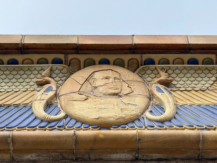 Color detail of the polychrome terra cotta that ornaments the raised parapet. This one is a doozy -- a winged roundel featuring a stylized pharaoh, along with some horizontal hieroglyphs. The cracked and damaged roundel is flanked by two upright and menacing uraei cobras wearing crowns and facing opposite directions. The layered wings are rendered in three different colors and two different patterns and themselves sit on another bed of polychrome terra cotta that makes up the cornice.