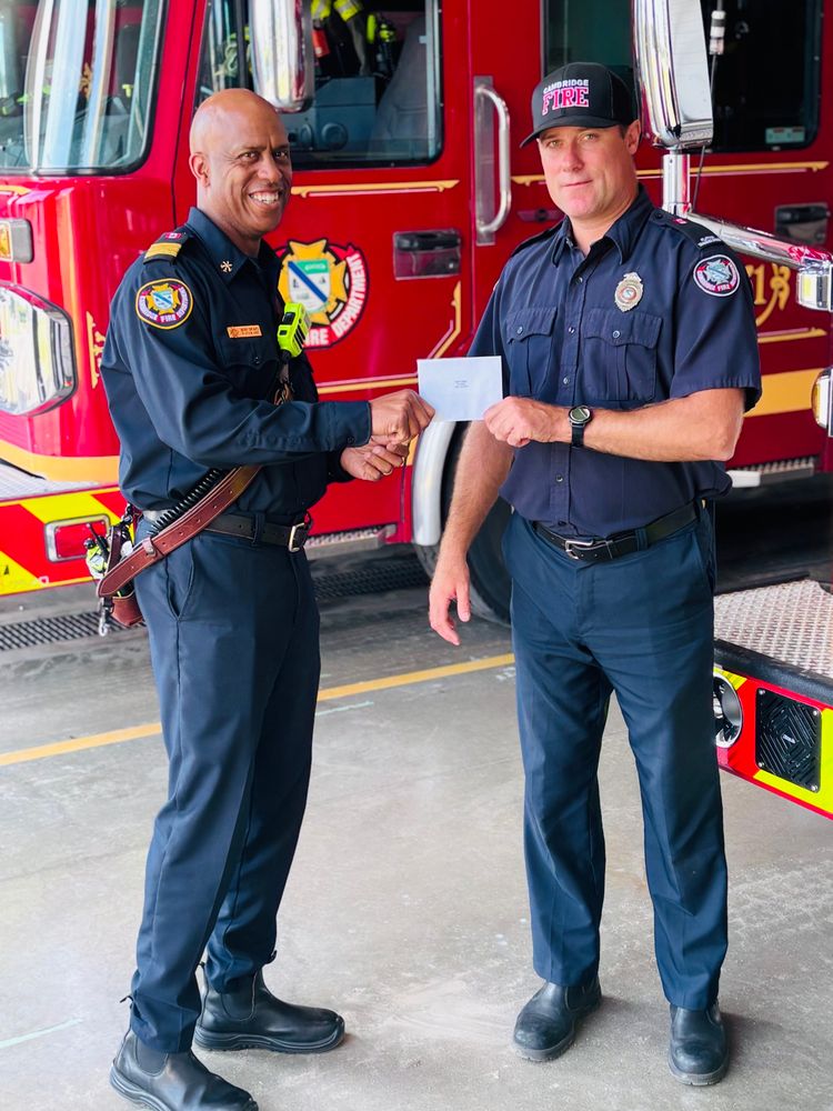 Platoon Chief handing an envelope with a service bar for 15 years of service to a 
Platoon Training Officer Firefighter 