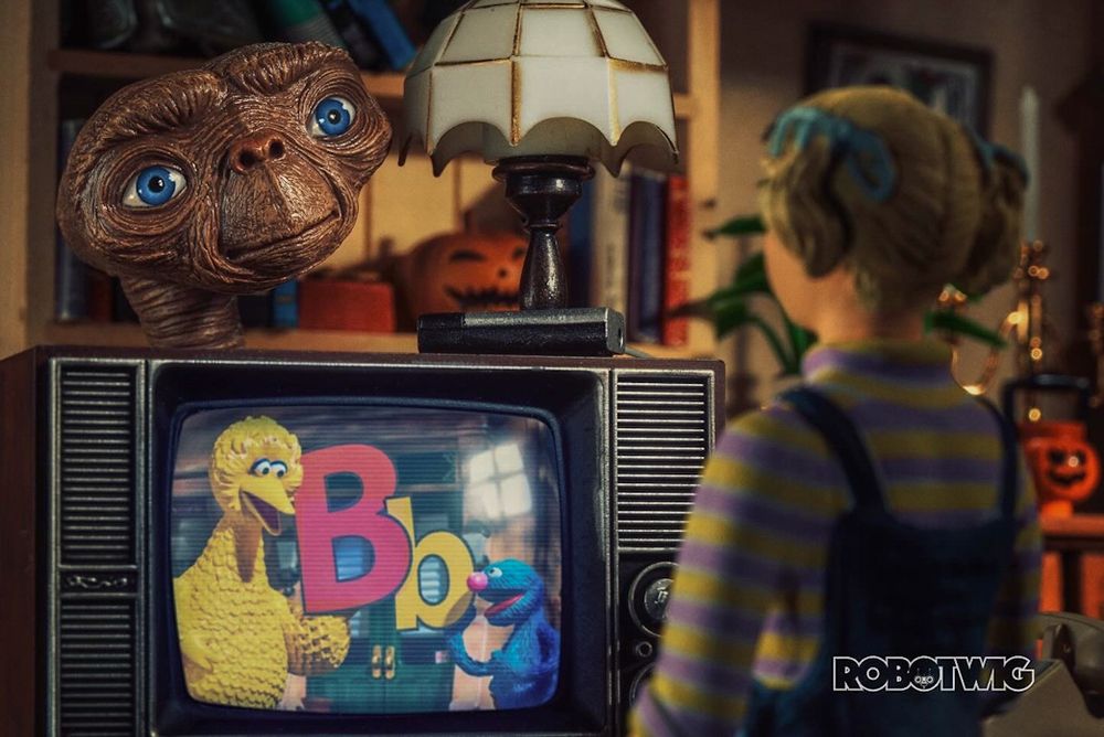 E.T appears from behind a TV Gertie is watching Sesame Street. Big bird and Grover are holding the letters B