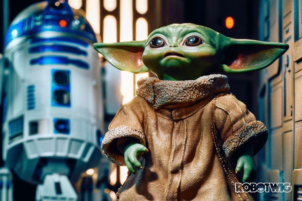 Grogu looks up at the Mandalorian who's out of shot. R2D2 stands behind him