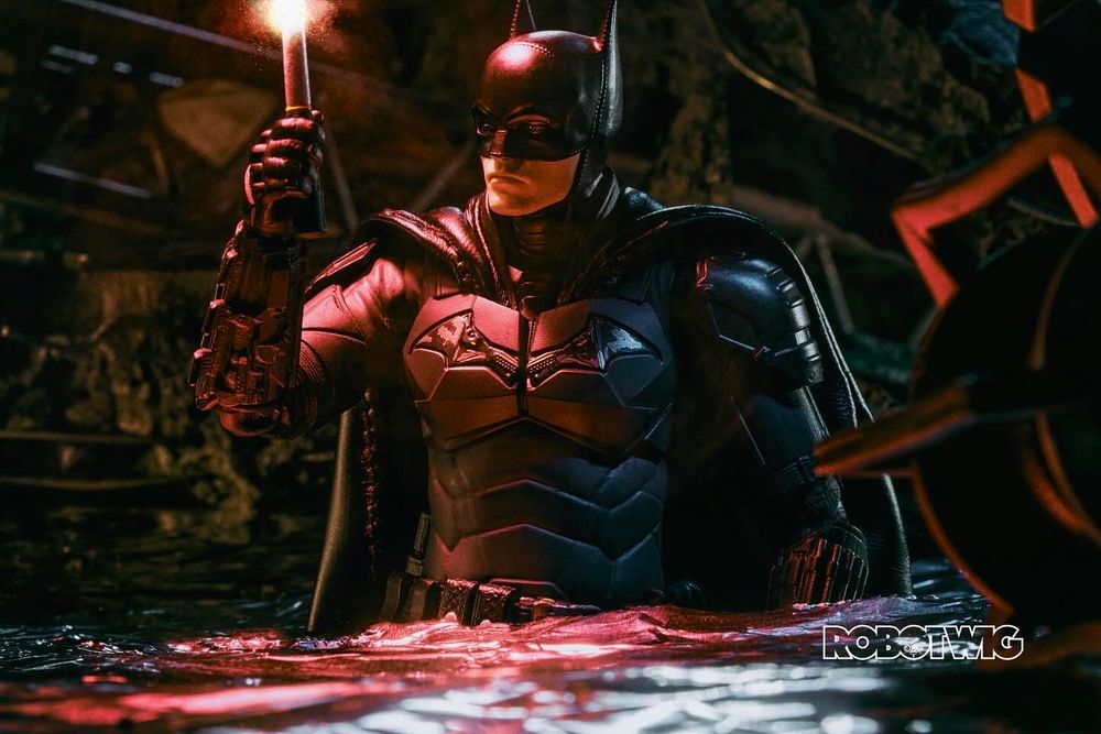 Batman wades in water and through rubble holding a flare to light his way