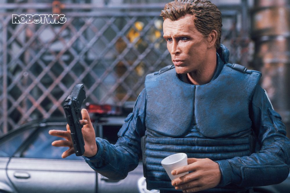 Murphy spins his gun in his hand, cop car and industrial fencing can be seen in the background 