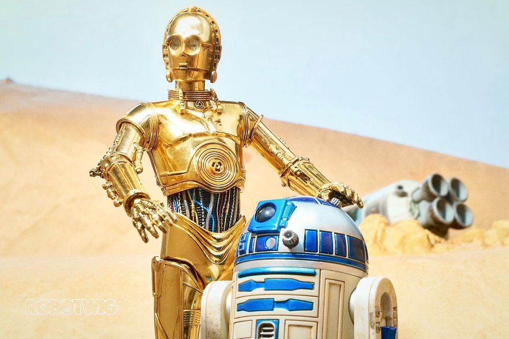 R2D2 and C3PO stand together in the desert, crashed escape pod behind them