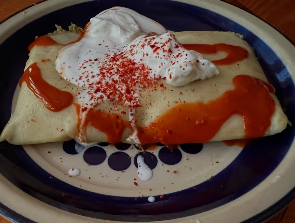 A tamale with sour cream and hot sauce and sprinkled with a little Aleppo pepper on a blue and white plate from the mid 70s 