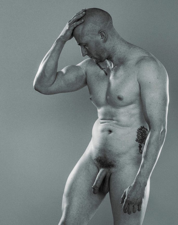 Male model standing, twisting to left of frame, right hand on head.