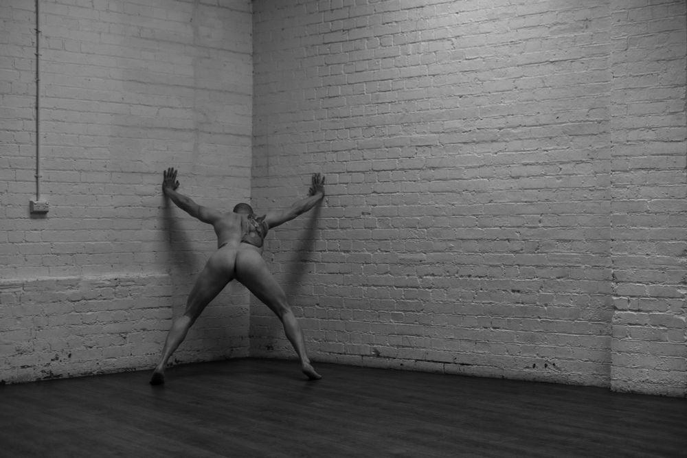 Male model leaning against the wall facing away from the viewer 