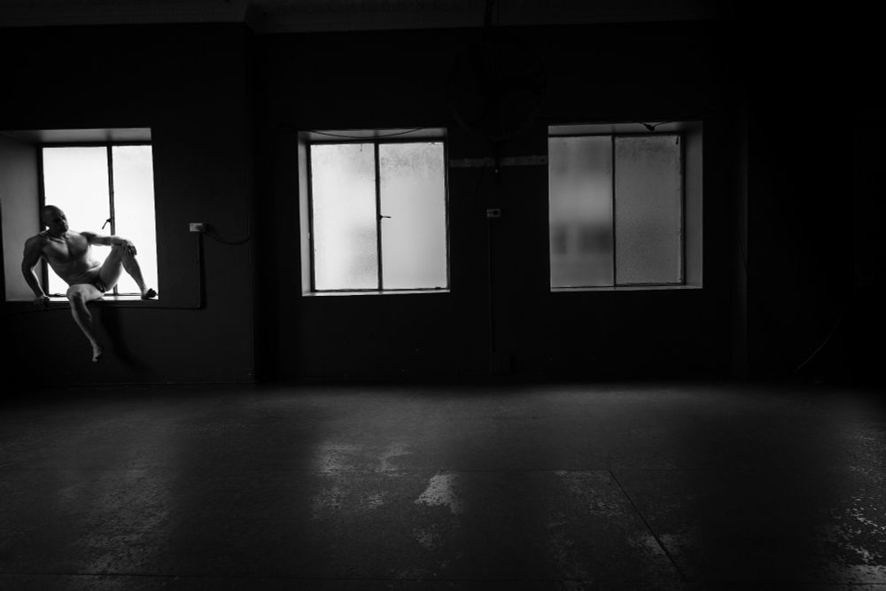 Male model perched open legged on the far left of frame windowsill 