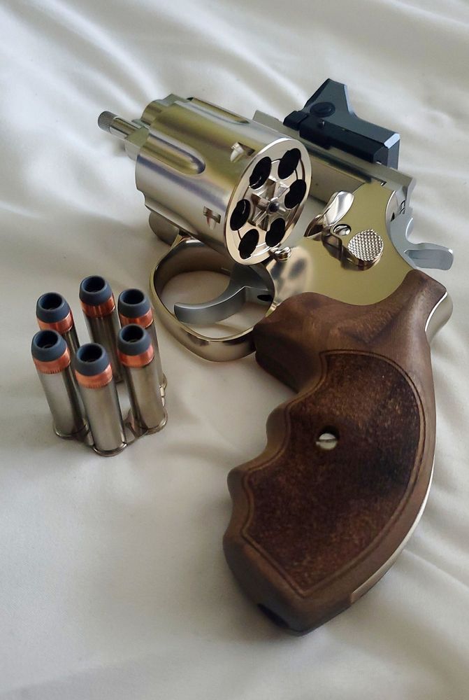 A chromed revolver with a small rds on a top rail, the cylinder is flipped open and shells are displayed alongside it in a moonclip