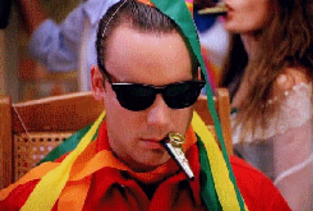 a man wearing sunglasses and a rainbow scarf is blowing a horn