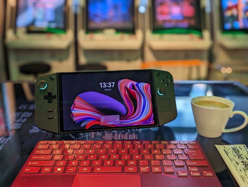 In a cafe with retro Arcade cabinets, handheld gaming PC and external keyboard, a cup of latte on the table