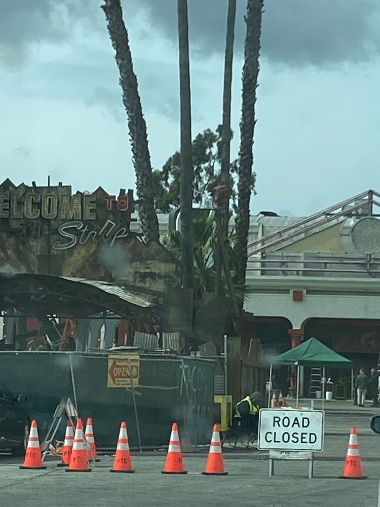 A long distance photo of a parking lot where a tv is being built. Next to 3 palm trees is a constructed metal scrap sign that says “Welcome to the Strip”. 