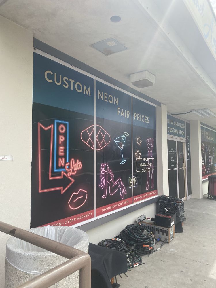 Large windows from the tv filming set, showing posters advertising a custom neon shop. 