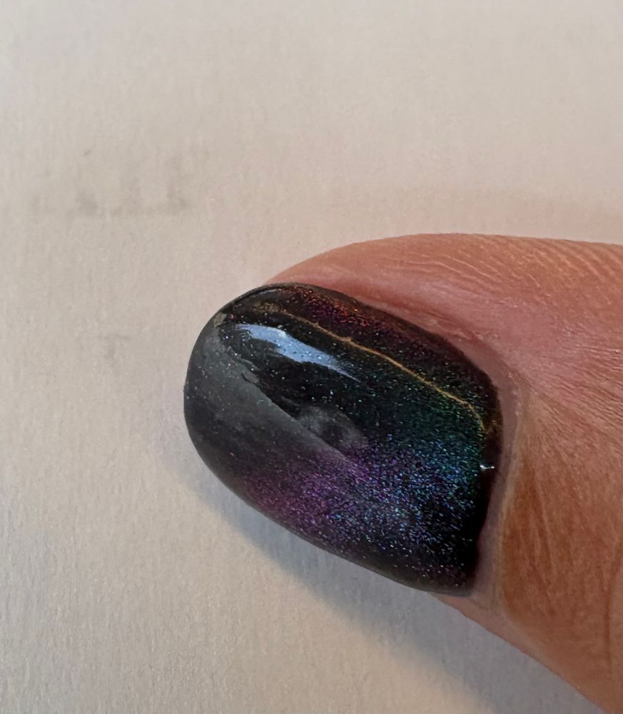 Close up of a thumb nail with black, purple, blue galaxy-effect nail polish 