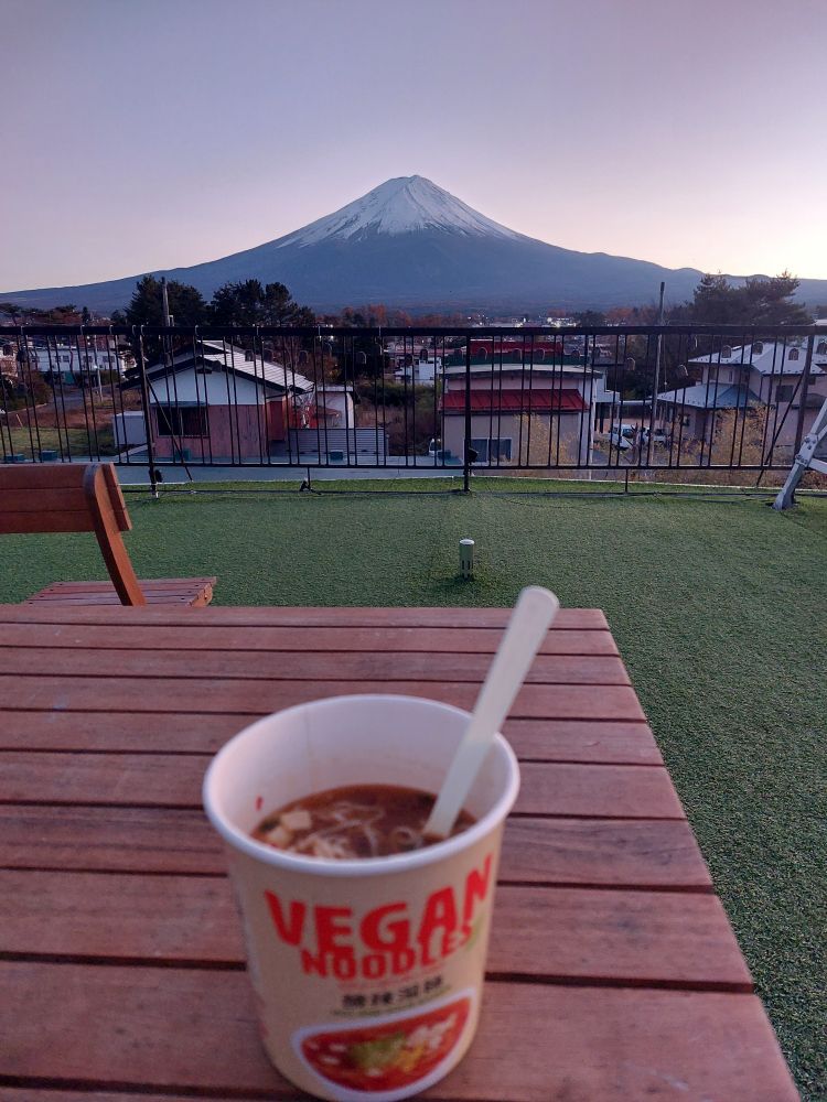 A cup of vegan instant noodles on a table overlooking Mt. Fuji at sunset.