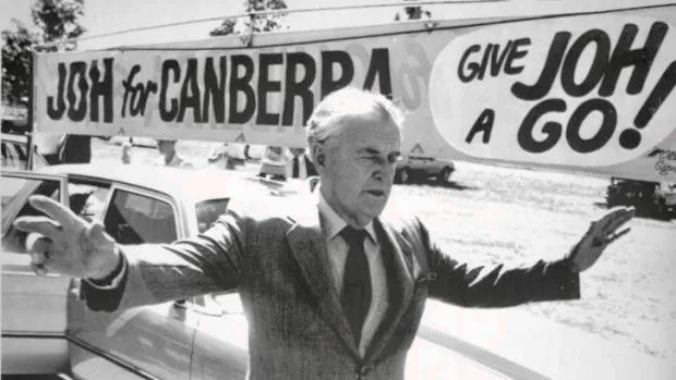 Queensland Premier Joh Bjelke-Petersen standing with arms outstretched in front of a banner sign reading ‘Joh for Canberra … Give Joh a Go’, early 1987 