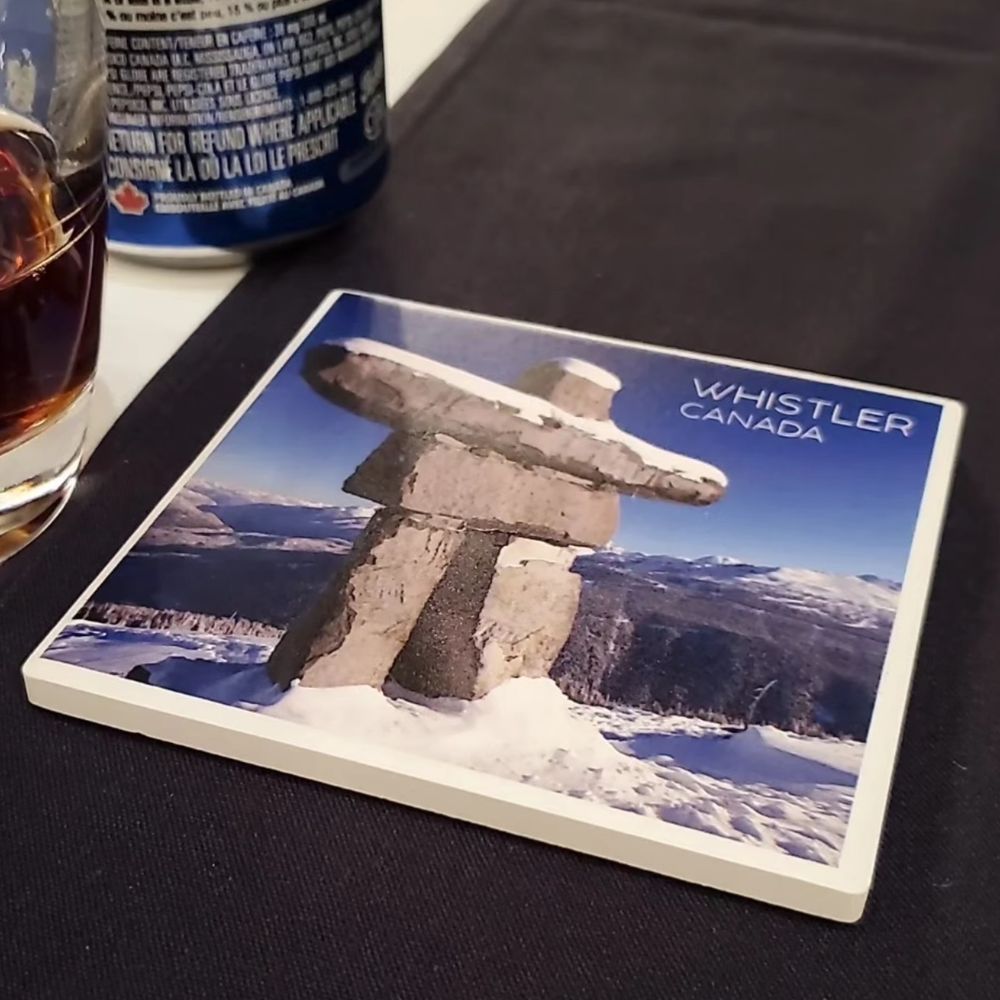 my reward for winning musical bingo: a coaster that says Whistler, Canada with a picture of the Whistler Mountain Inukshuk
