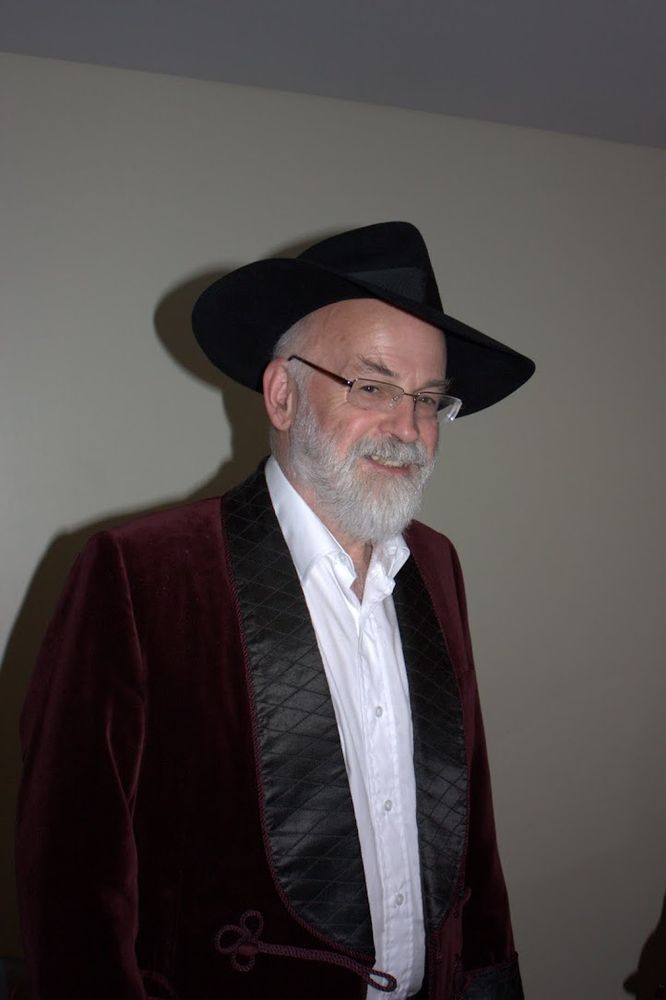 Sir Terry wearing a velvet jacket with white shirt open at the neck and his trademark hat