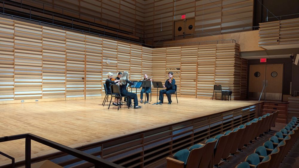 A strong quintet performs on a light colored wooden stage. There are two violinists, a cellist and two violists