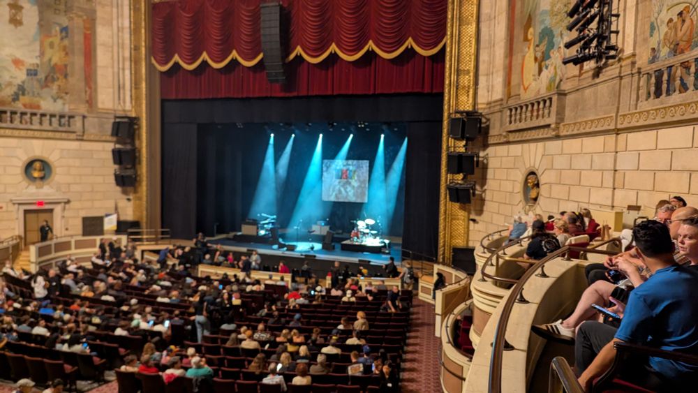 People file into their seats with a grand older theater stage ahead