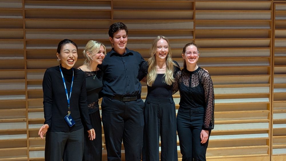 Four people dressed on black pose for a group photo 