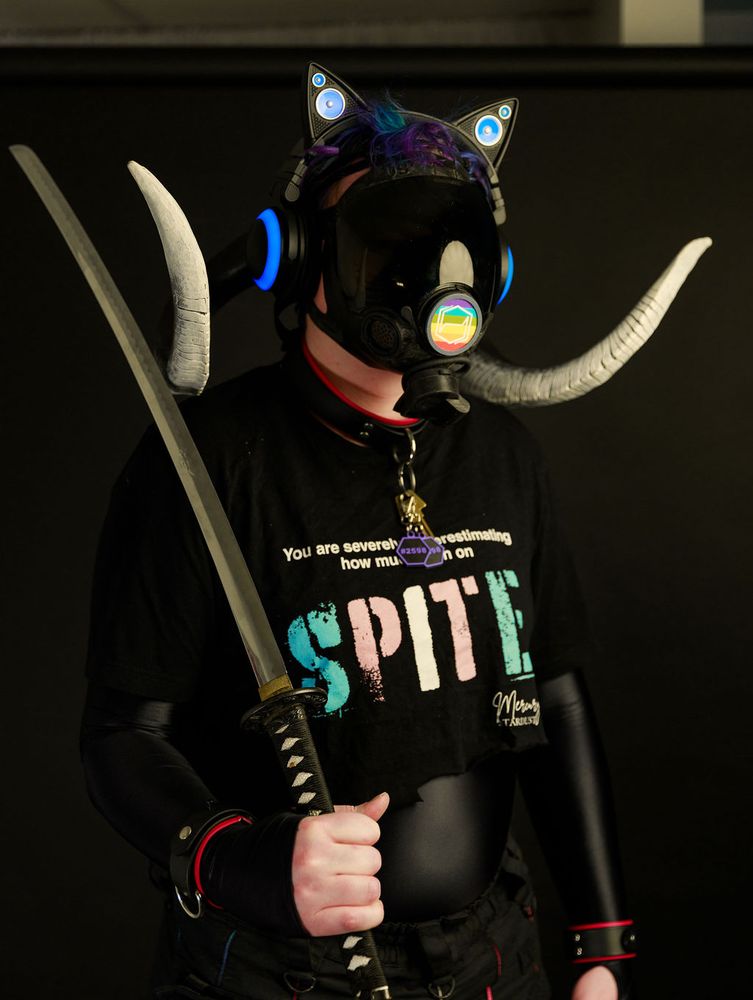 2598 standing at attention yet relaxed. It is looking off in no discernable direction, light reflecting off of its visor and making it's spandex suit shine. The drone is also holding a sword against it's right shoulder