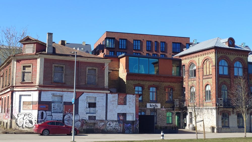 A row of mixed style buildings made of red brick, the bottom row features graffito of big white bulky letters