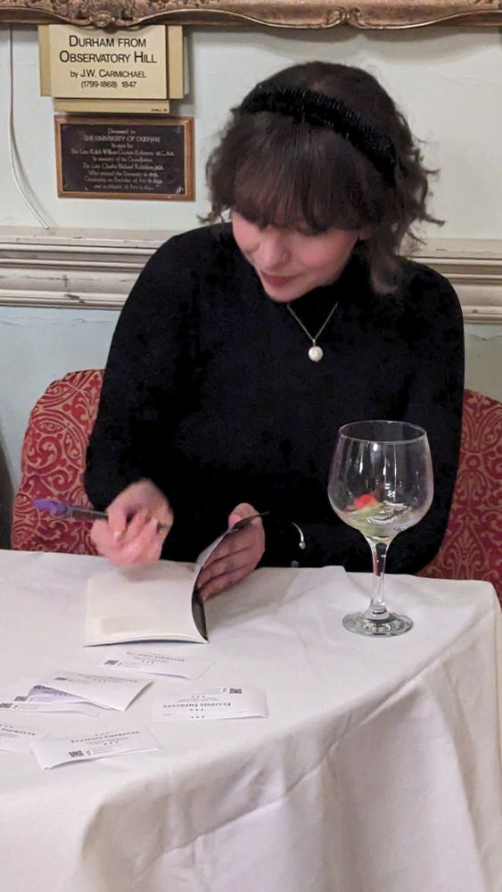 A white woman with dark wavy hair dressed in black sitting at table signing copies of her books.