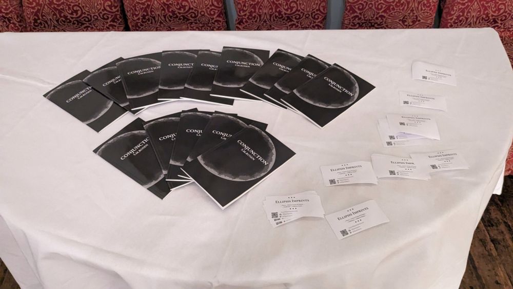 A white table cloth with black books arranged in two arcs, with white business cards scattered on the side.