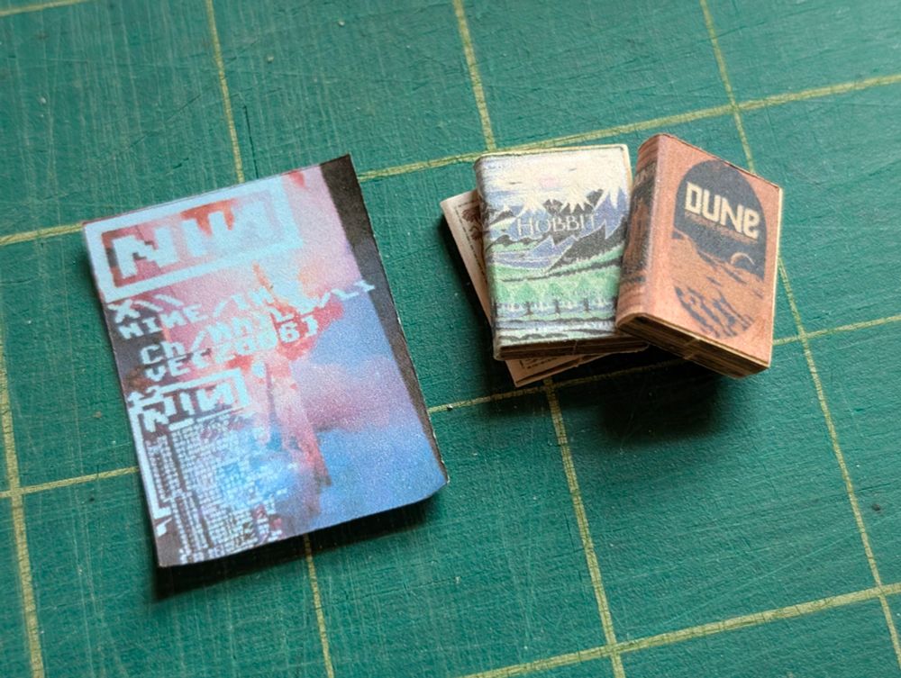 small book models, but one with a tiny print version of the Dune hardcover, and another from The Hobbit. next to them is a tiny Nine Inch Nails 2006 tour poster