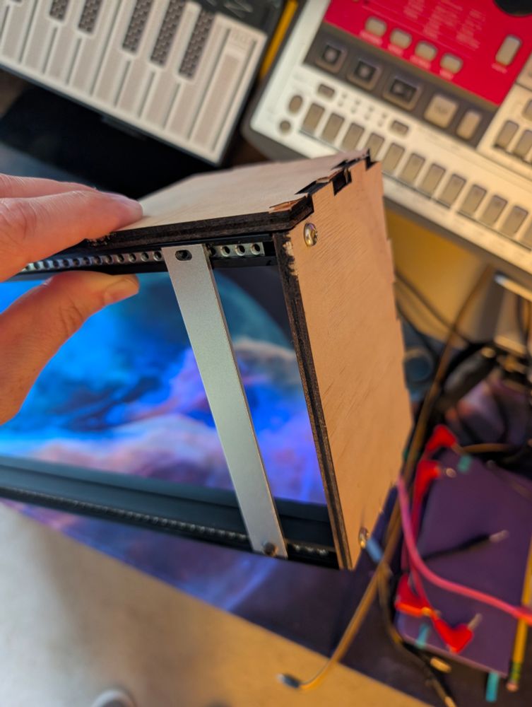 hand holding a wood plywood corner with rough finger joints, eurorack rails and blank panel screwed in 