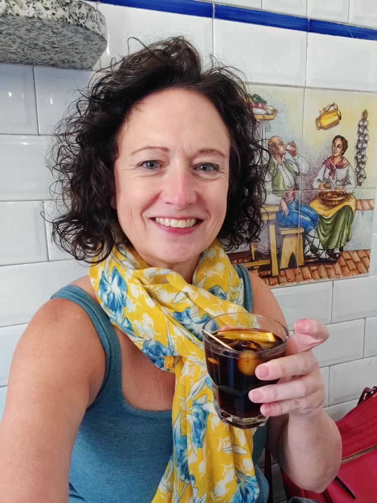 Me, a white woman smiling at the camera holding a glass of vermouth. I'm very tired.