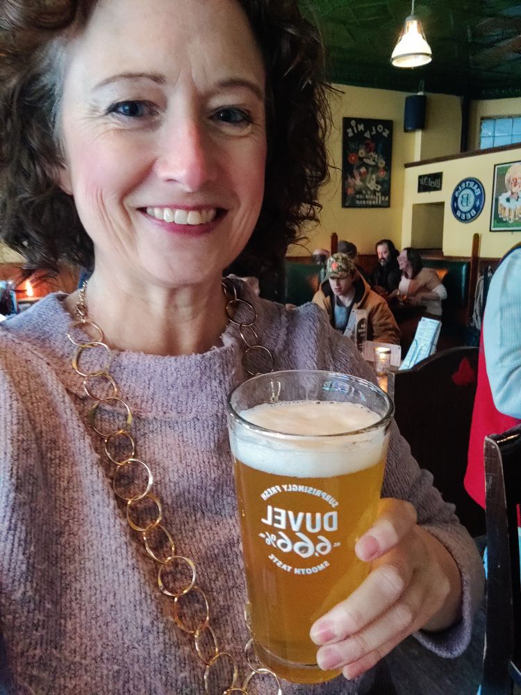 Me, a white woman, smiling at the camera holding a beer in a pint glass. 