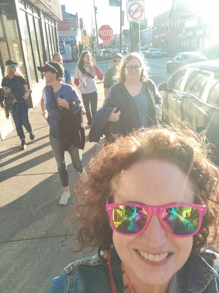 A group of people walking down the street. A selfie of me in front wearing pink sunglasses.