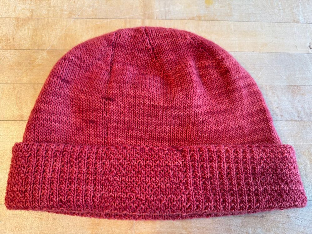 Dark pink knit reversible hat shown with stockinette on the body and varying texture of broken rib and miss stitch on the brim of the hat. 