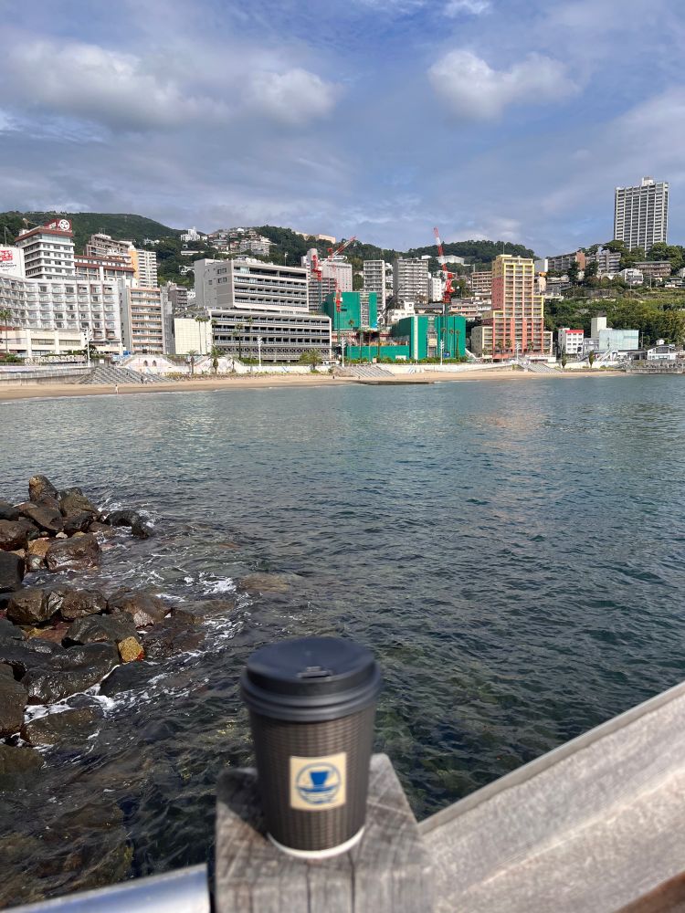 手前にコーヒーの入った紙コップ、奥に海と海辺のホテルが見える
