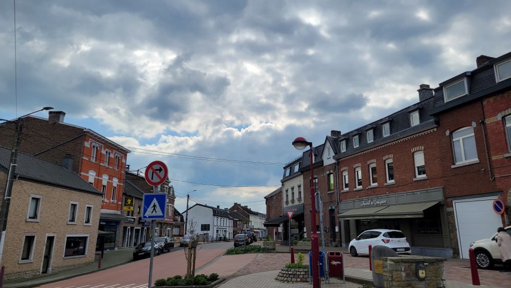 The same town. A crosswalk is to the left. A small sidewalk island is under the camera's viewpoint. The view is tilted upward. There's signage nearby.