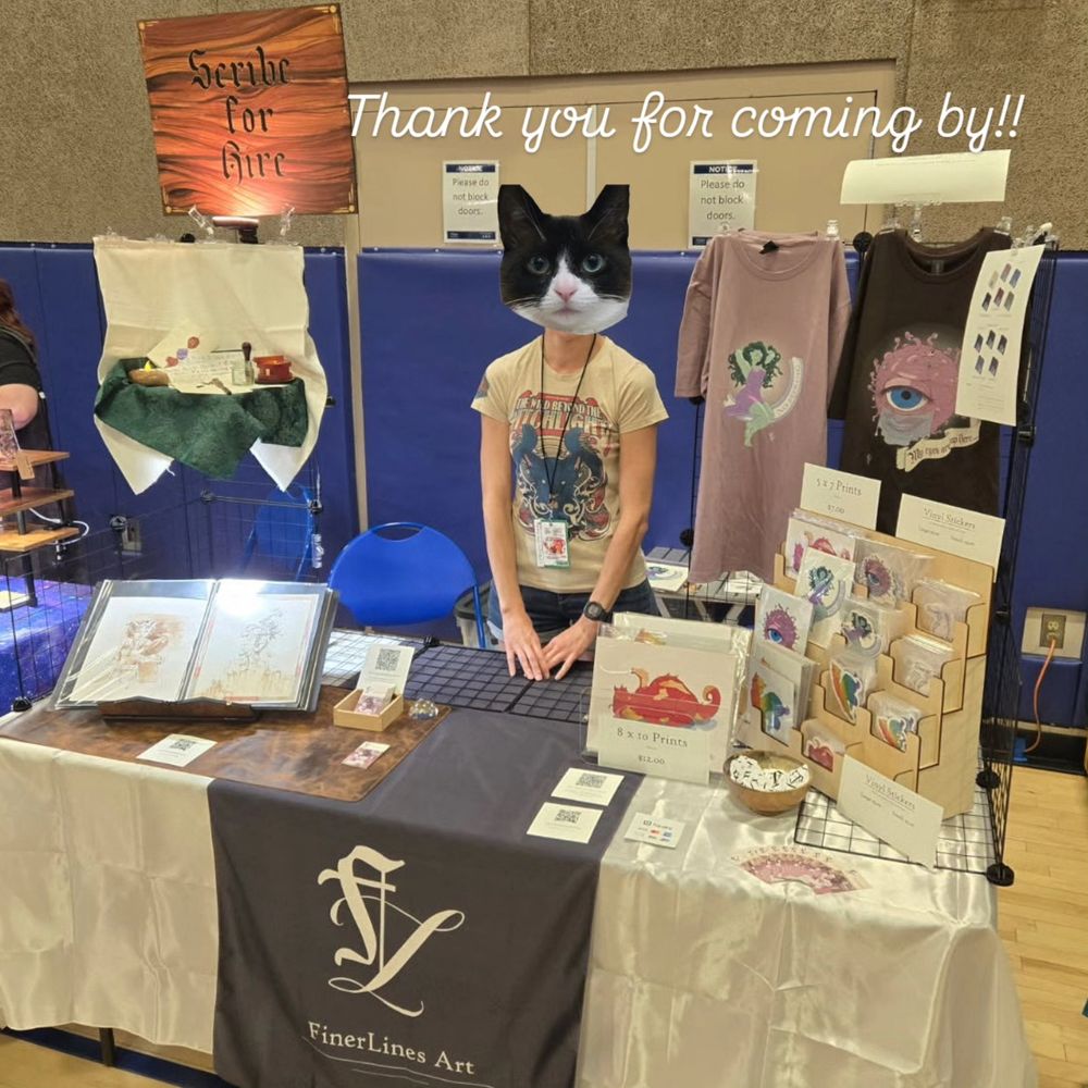 A comic convention booth with branding for Finer Lines Art. It has a large "Scribe for Hire" sign, a calligraphy equipment display, colorful fantasy stickers, two Dungeons & Dragons shirts, and a portfolio book with watercolor and ink art.