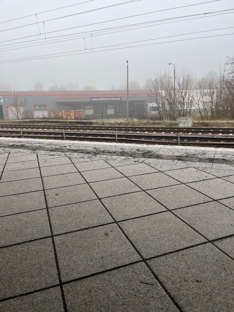 Blick von einem S-Bahnsteig auf ein trostloses Firmengebäude im Nebel.